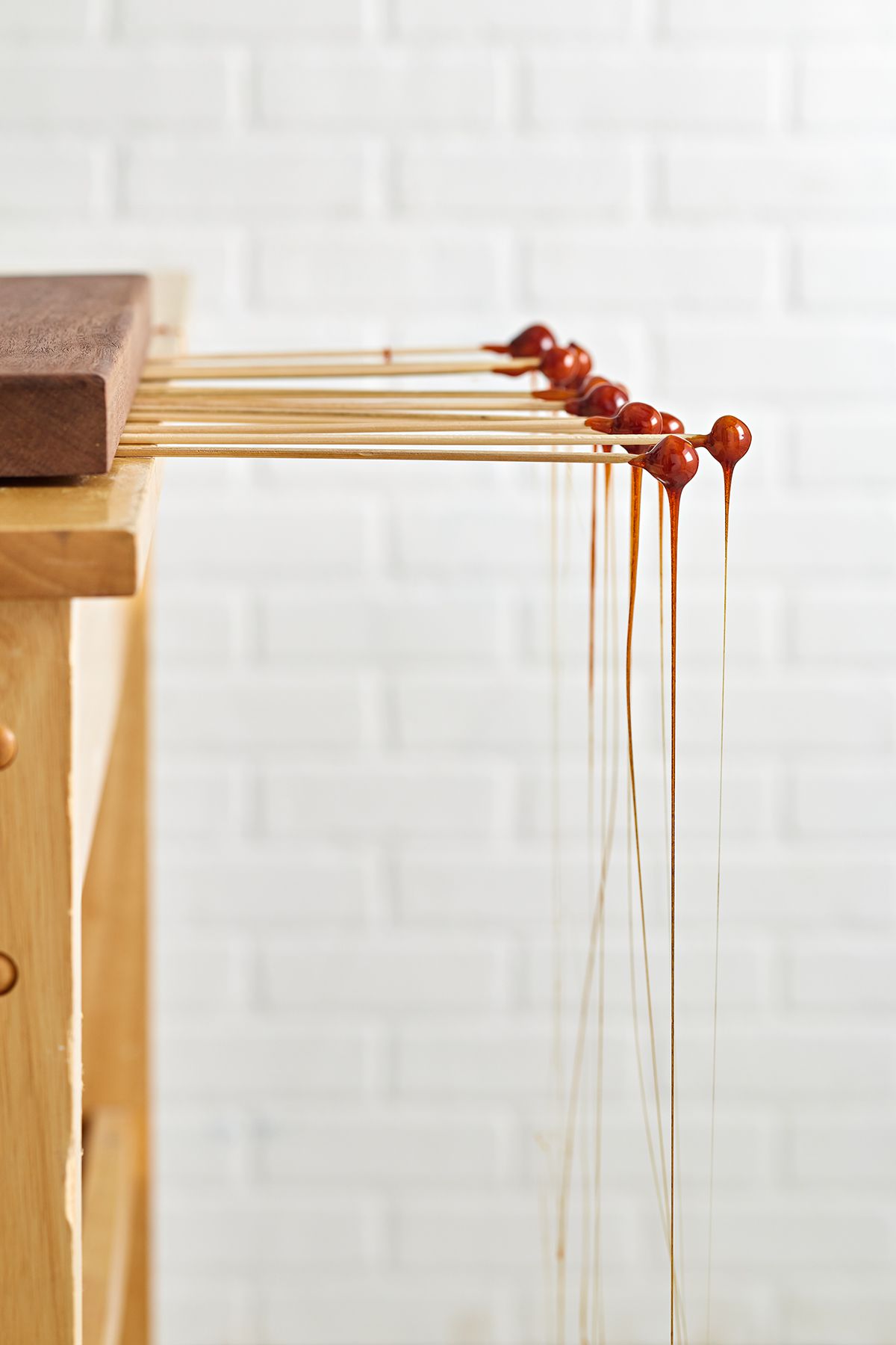 Hazelnuts on wooden skewers covered in caramel dripping onto the ground