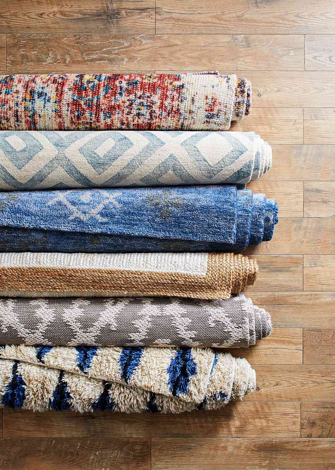 patterned blue, brown, and red rugs rolled on wooden floor