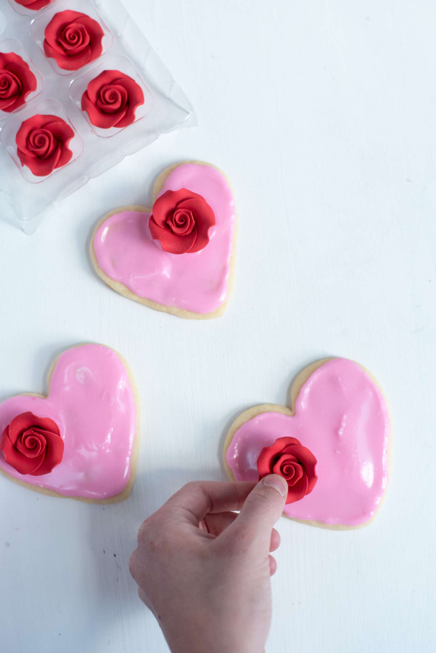 placing red sugar roses on heart-shaped iced cookies decorating