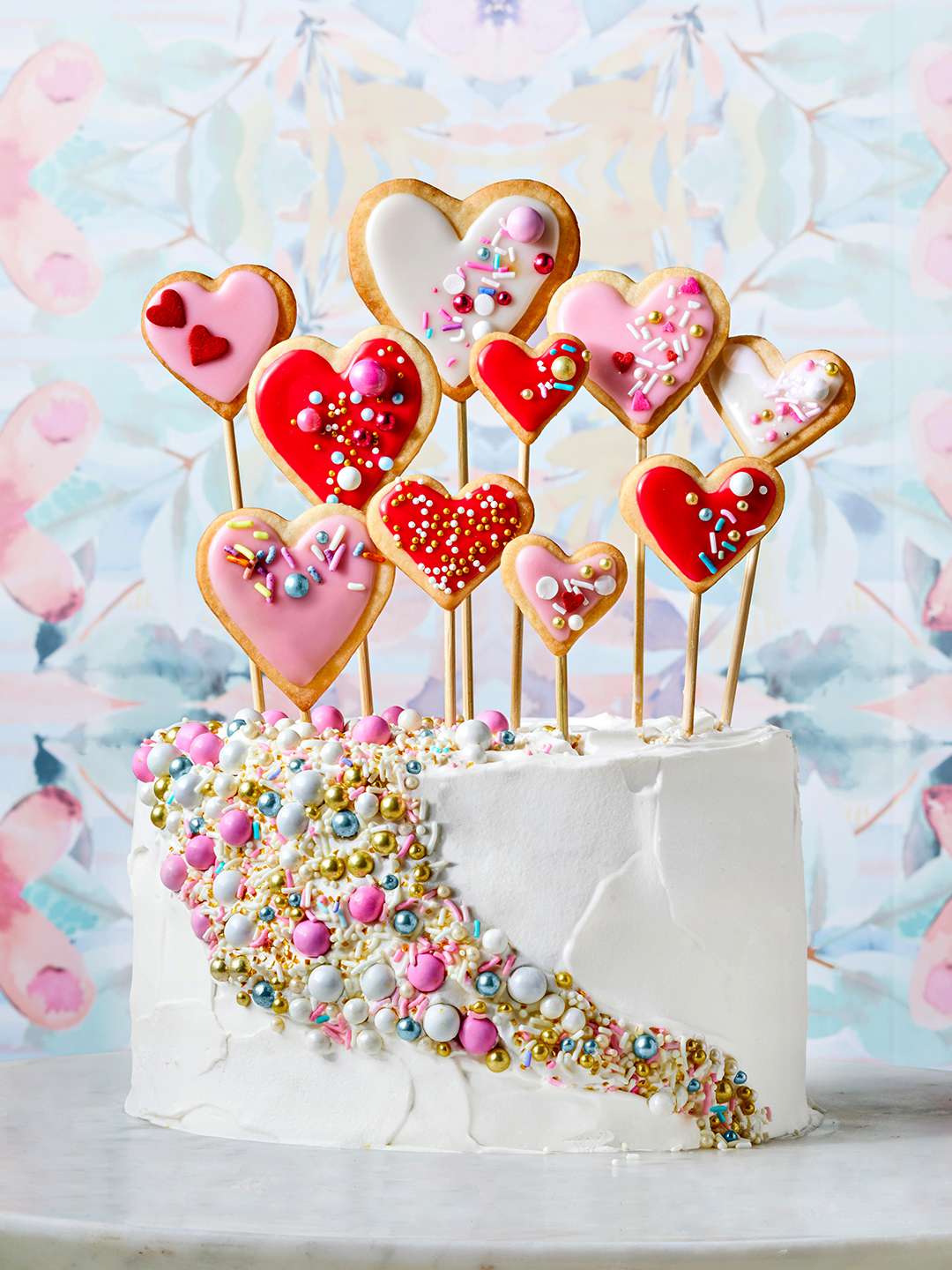 Valentine’s Cake topped with decorated heart-shaped cookies on a stick and a pattern of sprinkles