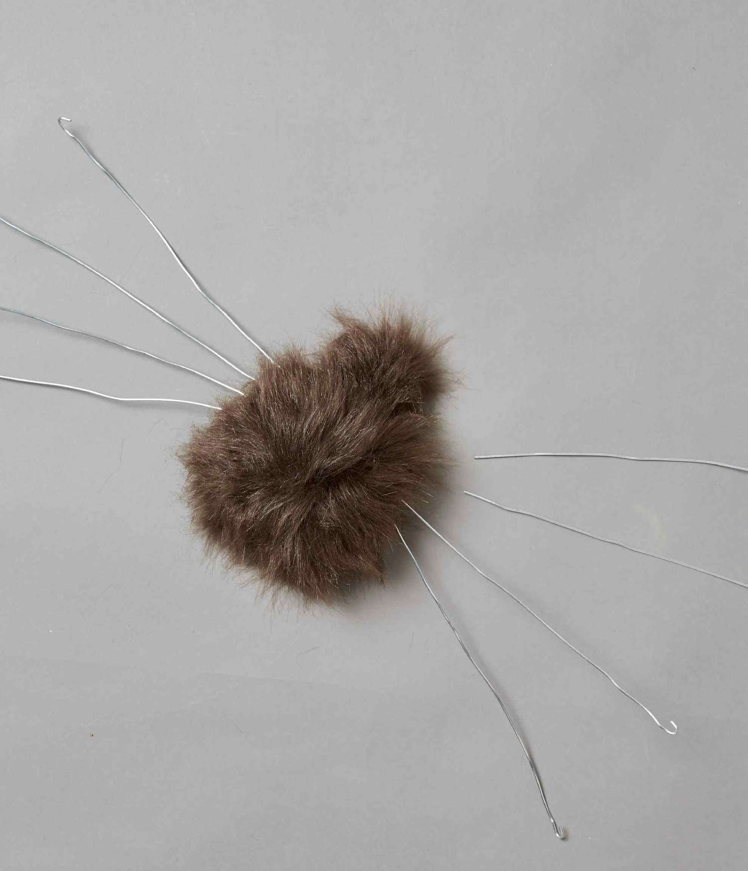 Fuzzy brown faux spider body with eight pieces of wire attached to the body