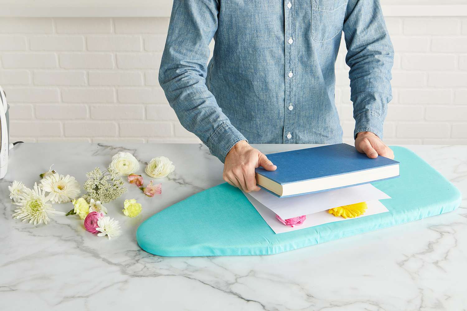 pressing flowers with book between paper sheets on ironing board