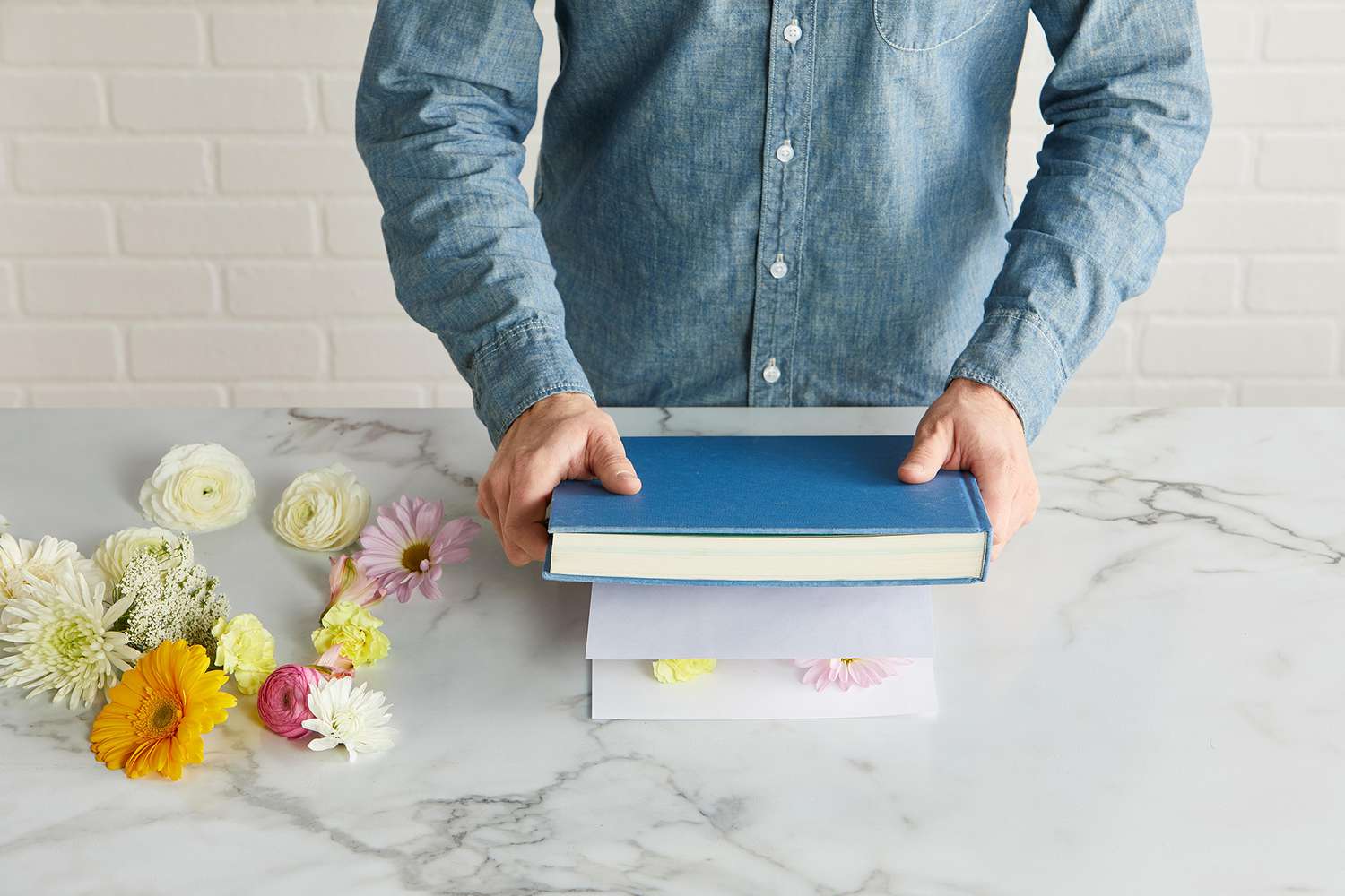 pressing flowers with blue covered book and paper sheets