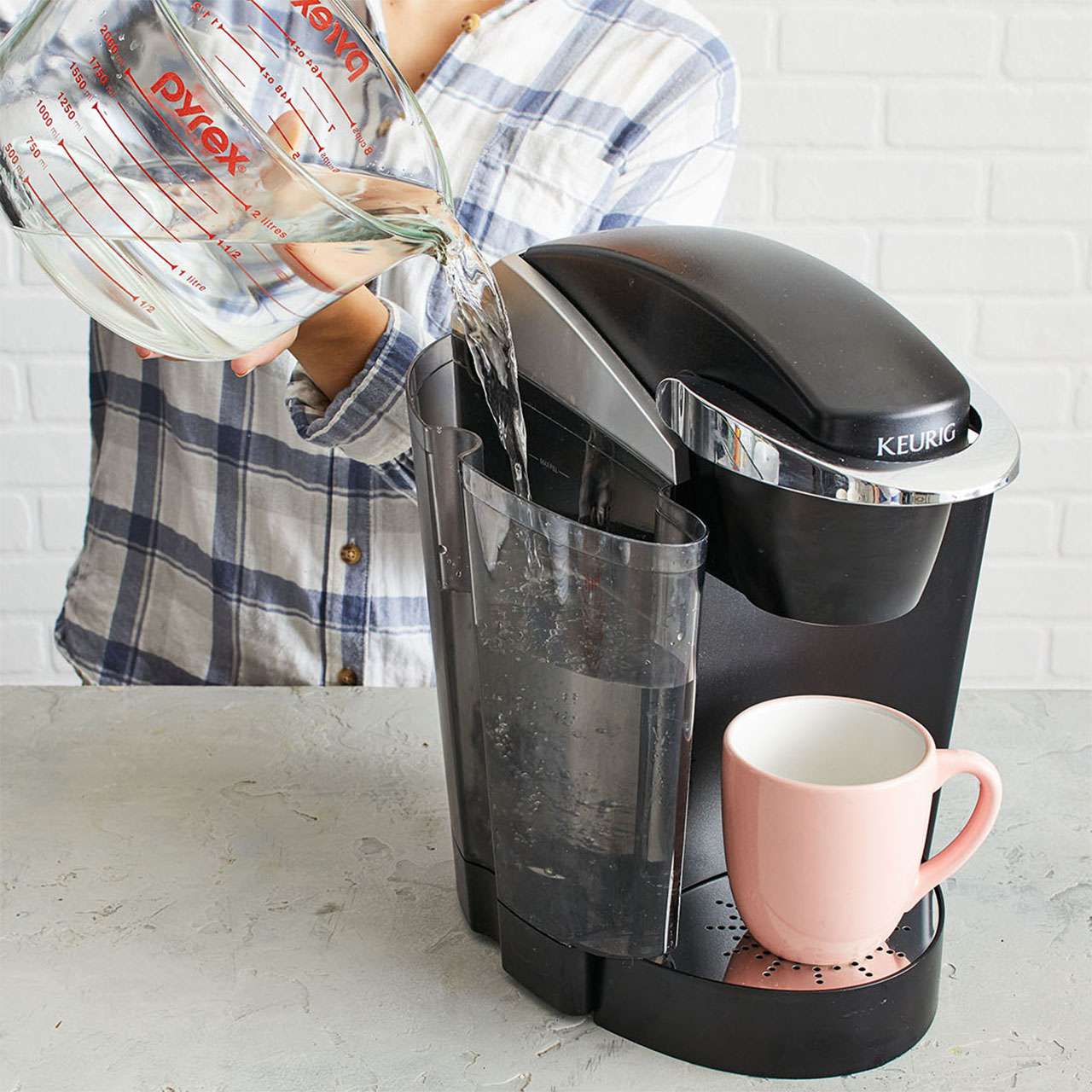 woman wearing plaid pouring water from pyrex measuring glass into keurig