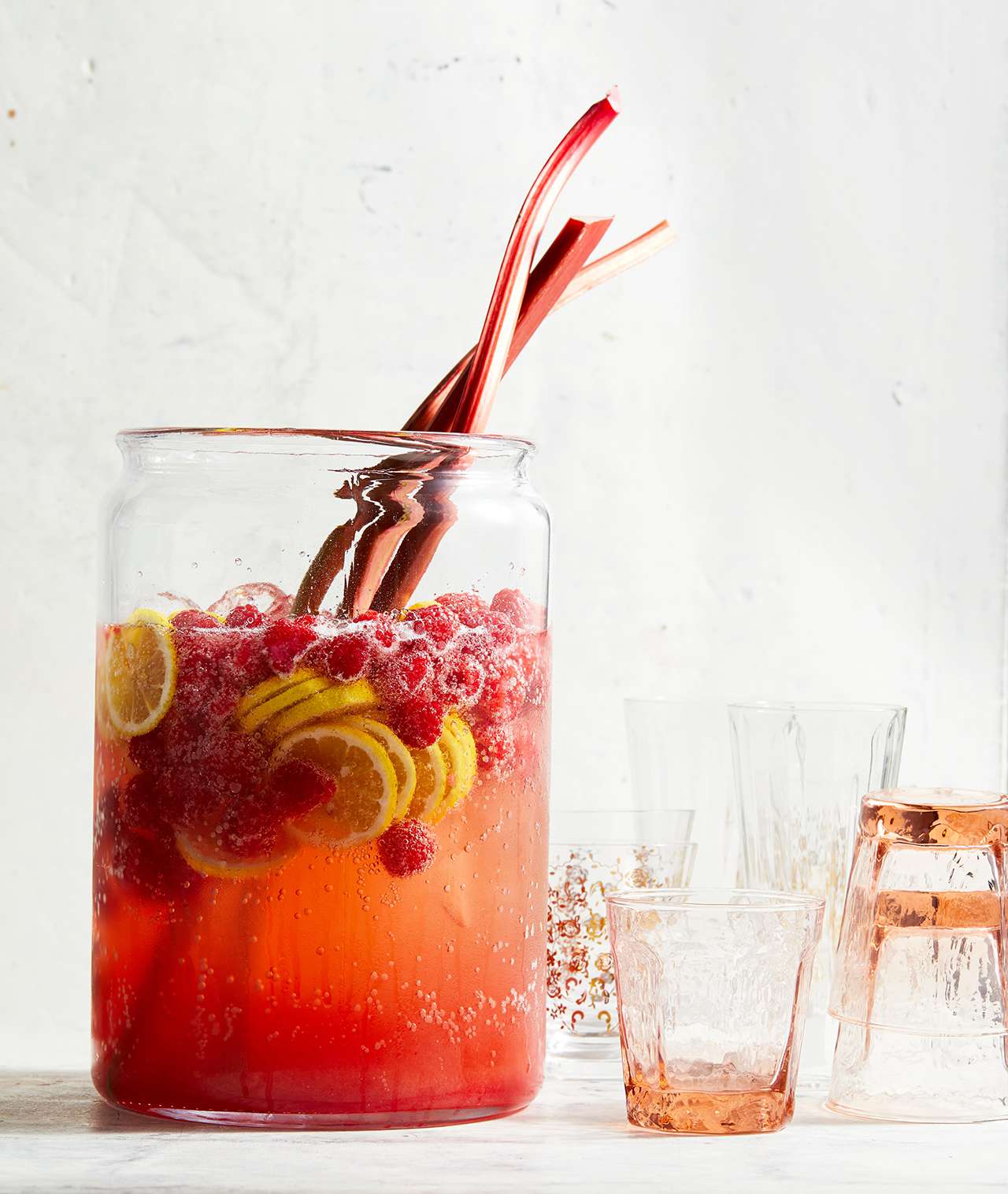 Ginger Rhubarb-Raspberry Punch in tall glass pitcher with drinking cups