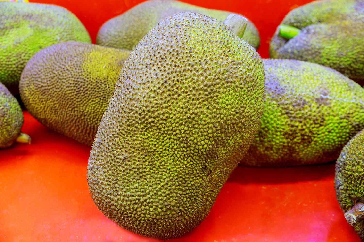 Several whole Jackfruits on a red-orange wooden surface