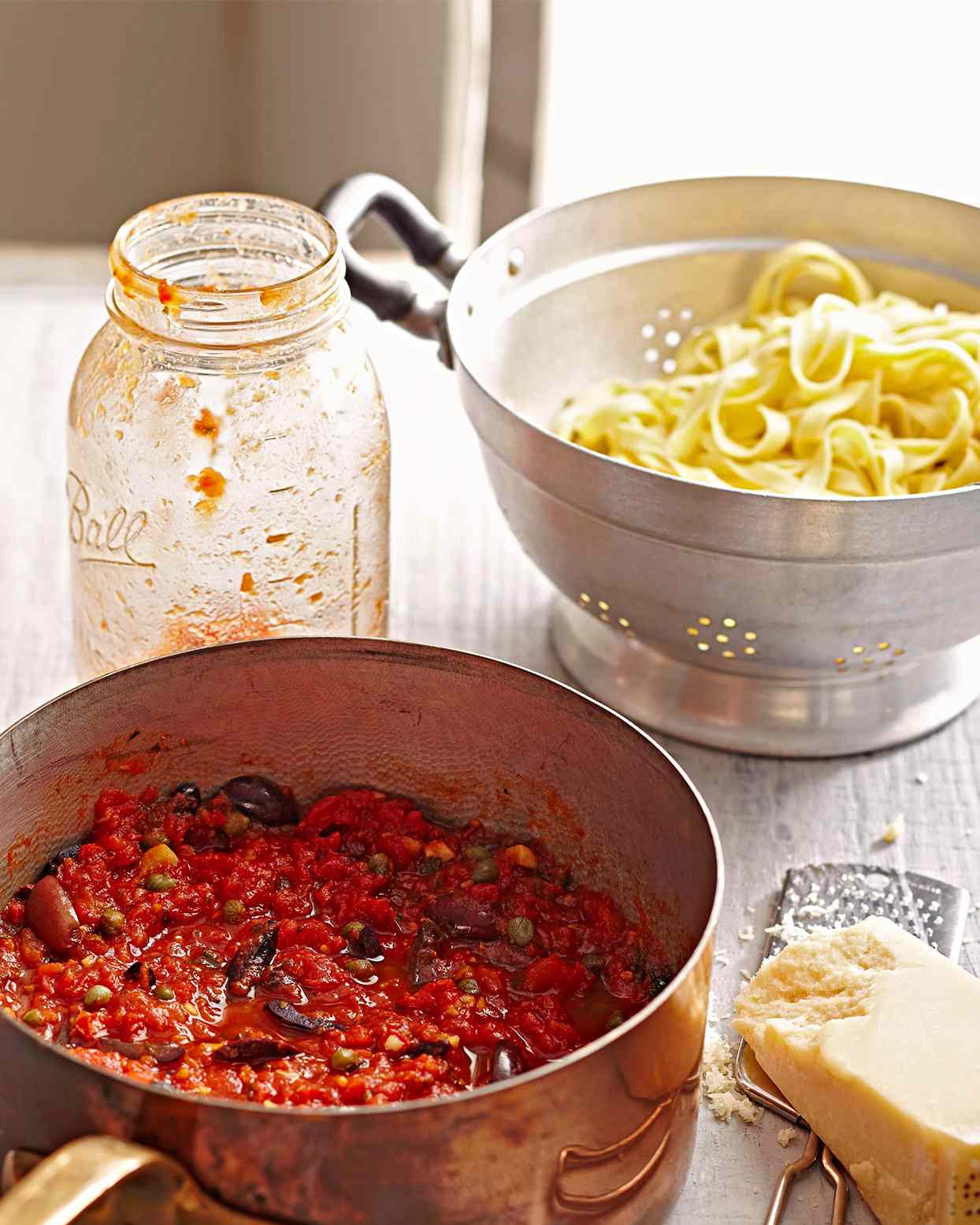 strainer full of cooked pasta next to pot of sauce