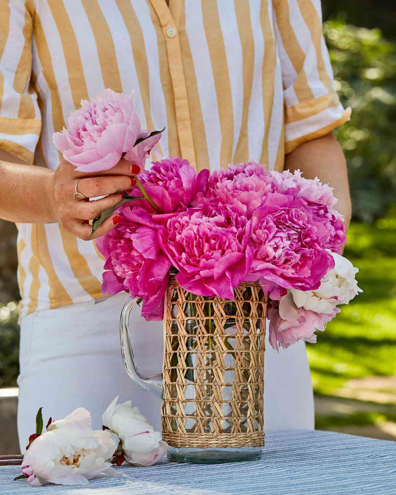 arranging peonies in glass pitcher outdoors