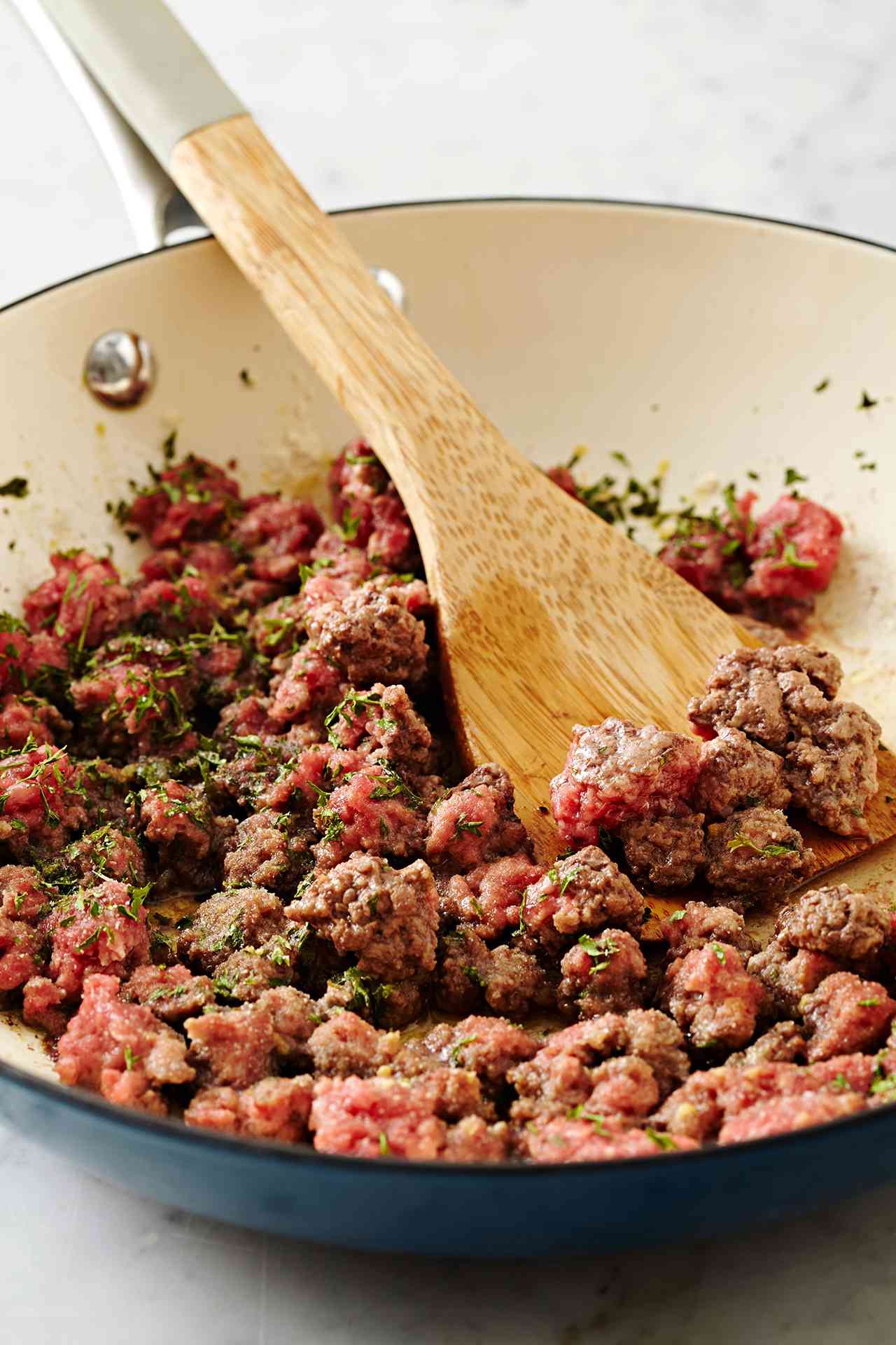browning ground beef in skillet with wood spoon