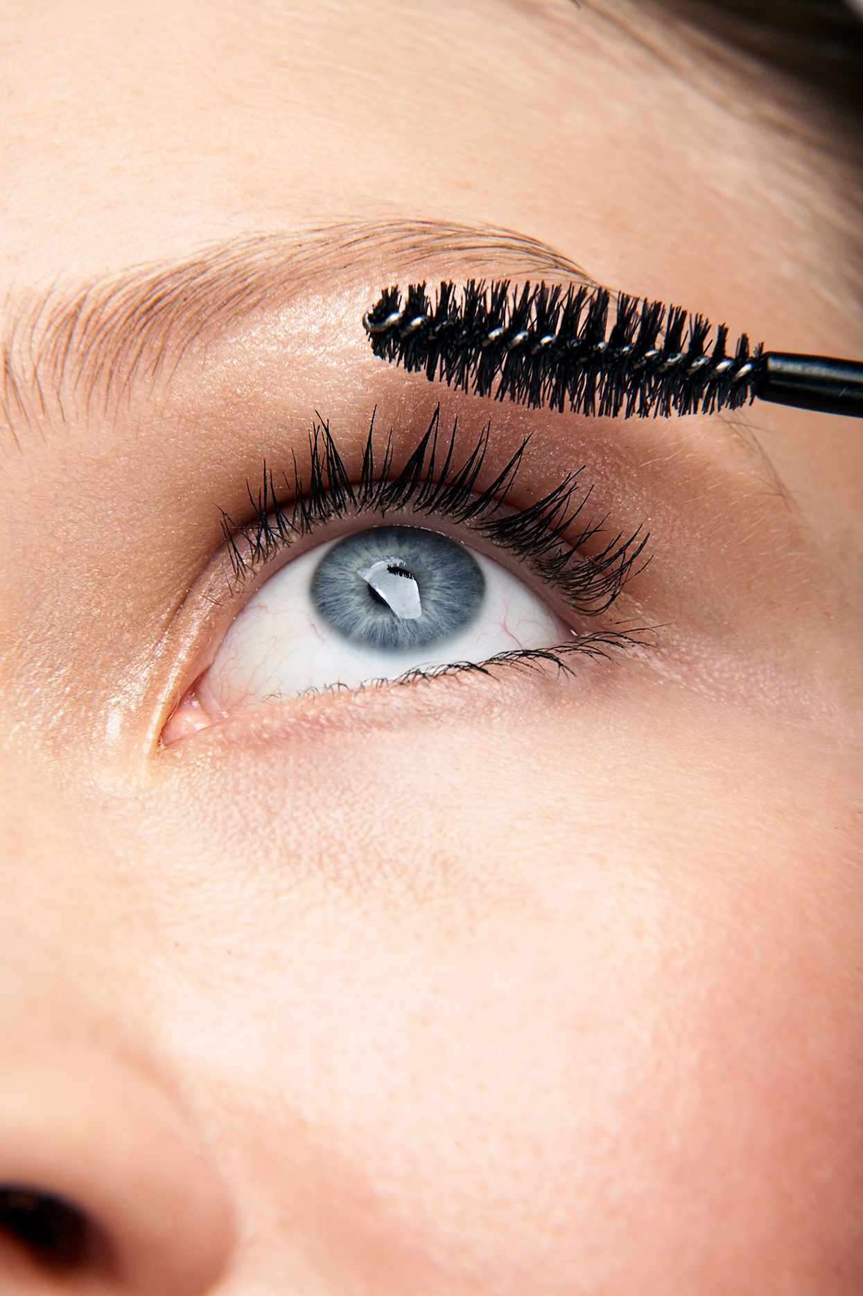blue-eyed woman applying mascara to eyelashes