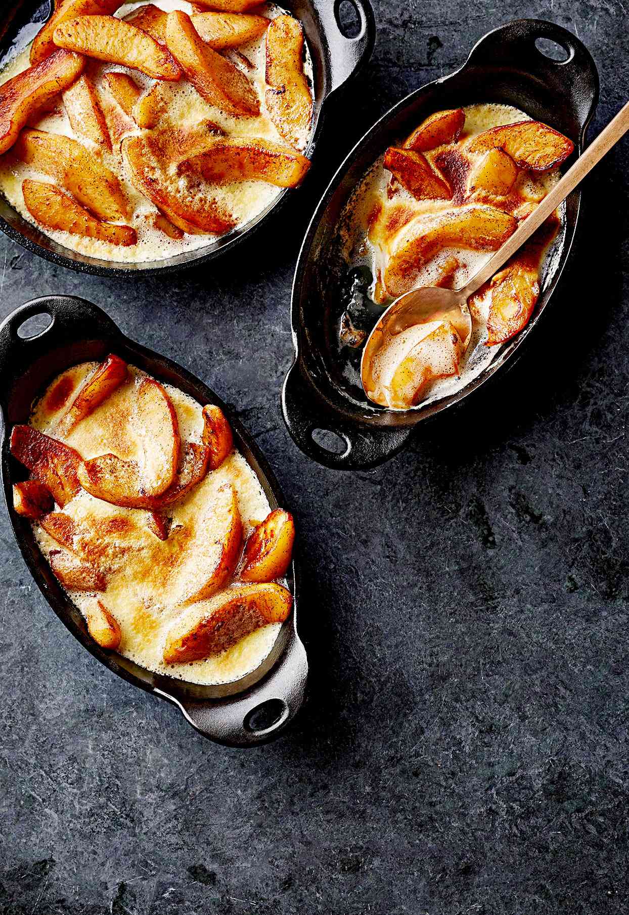 Vanilla apple gratin on dark surface in individual cast-iron gratin dishes