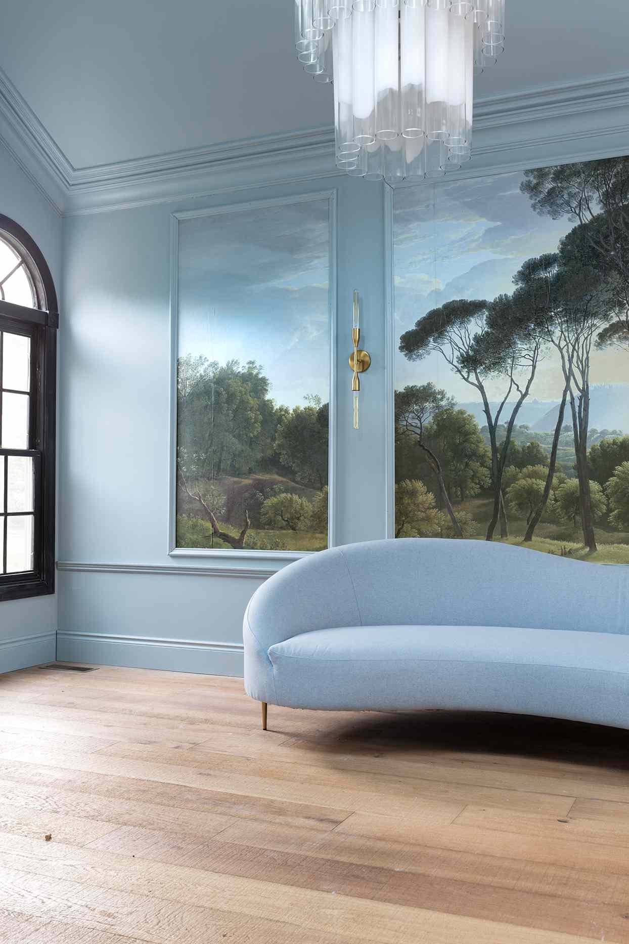 living room with curved light blue sofa and blue walls with landscape artwork