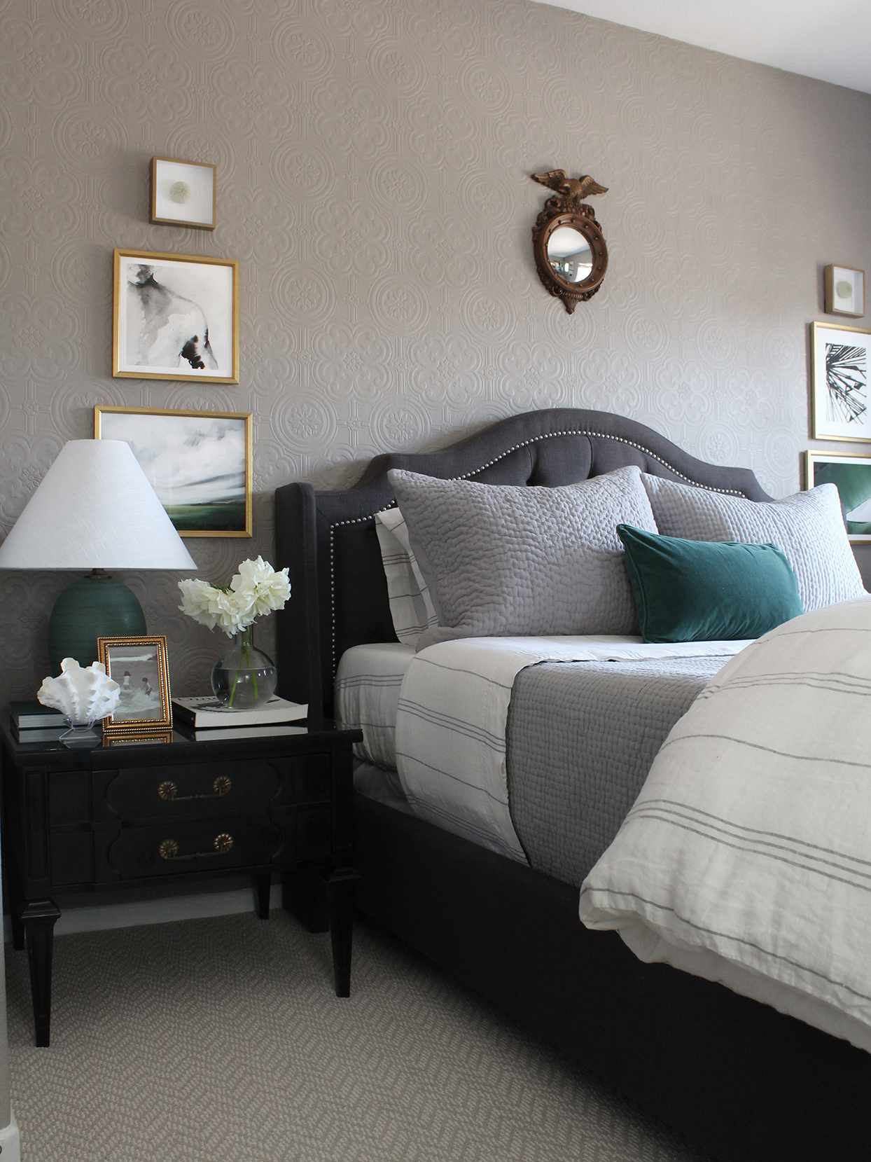 bedroom with gray walls gray headboard black nightstand with table lamp and gold-framed art hung on wall