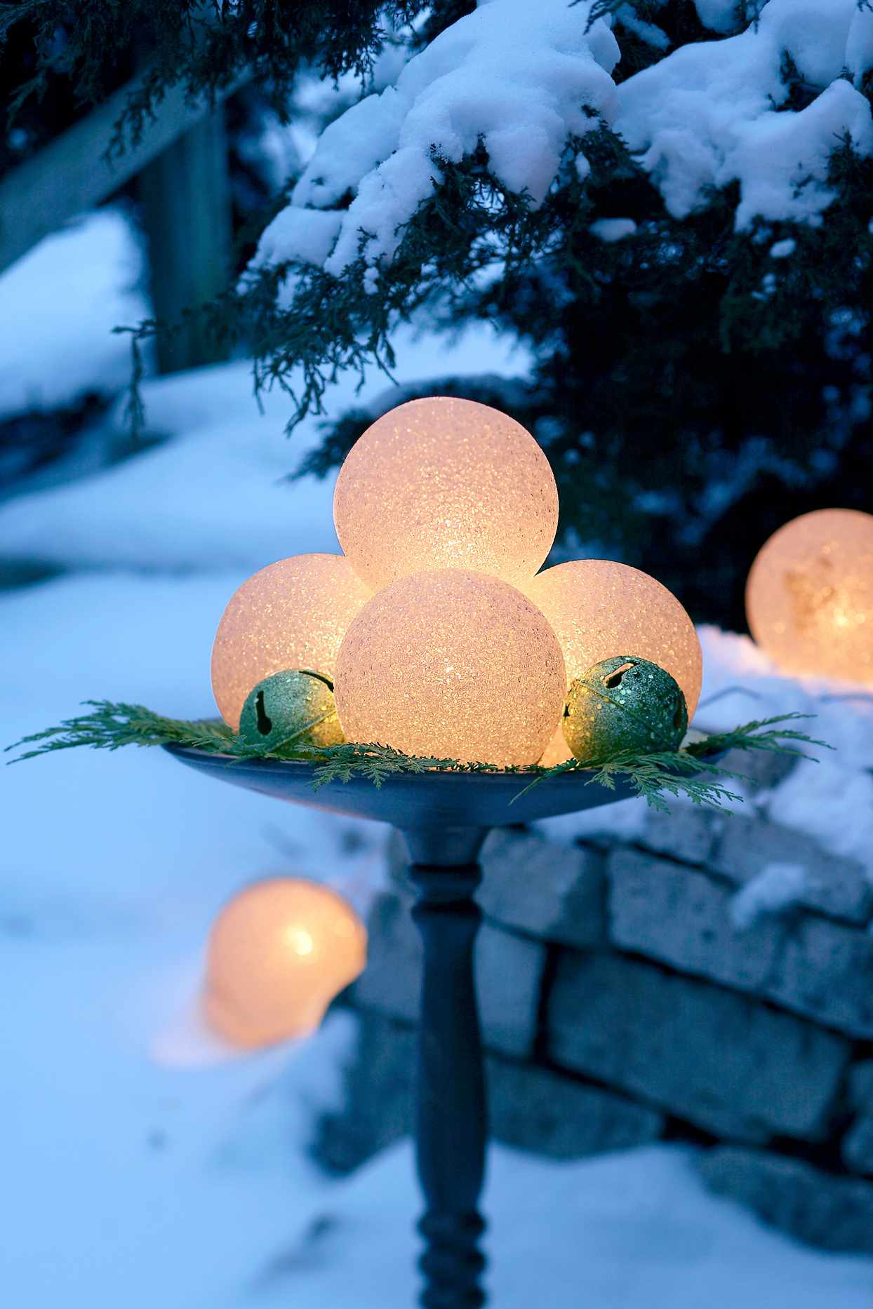 glowing holiday orbs atop snowy birdbath