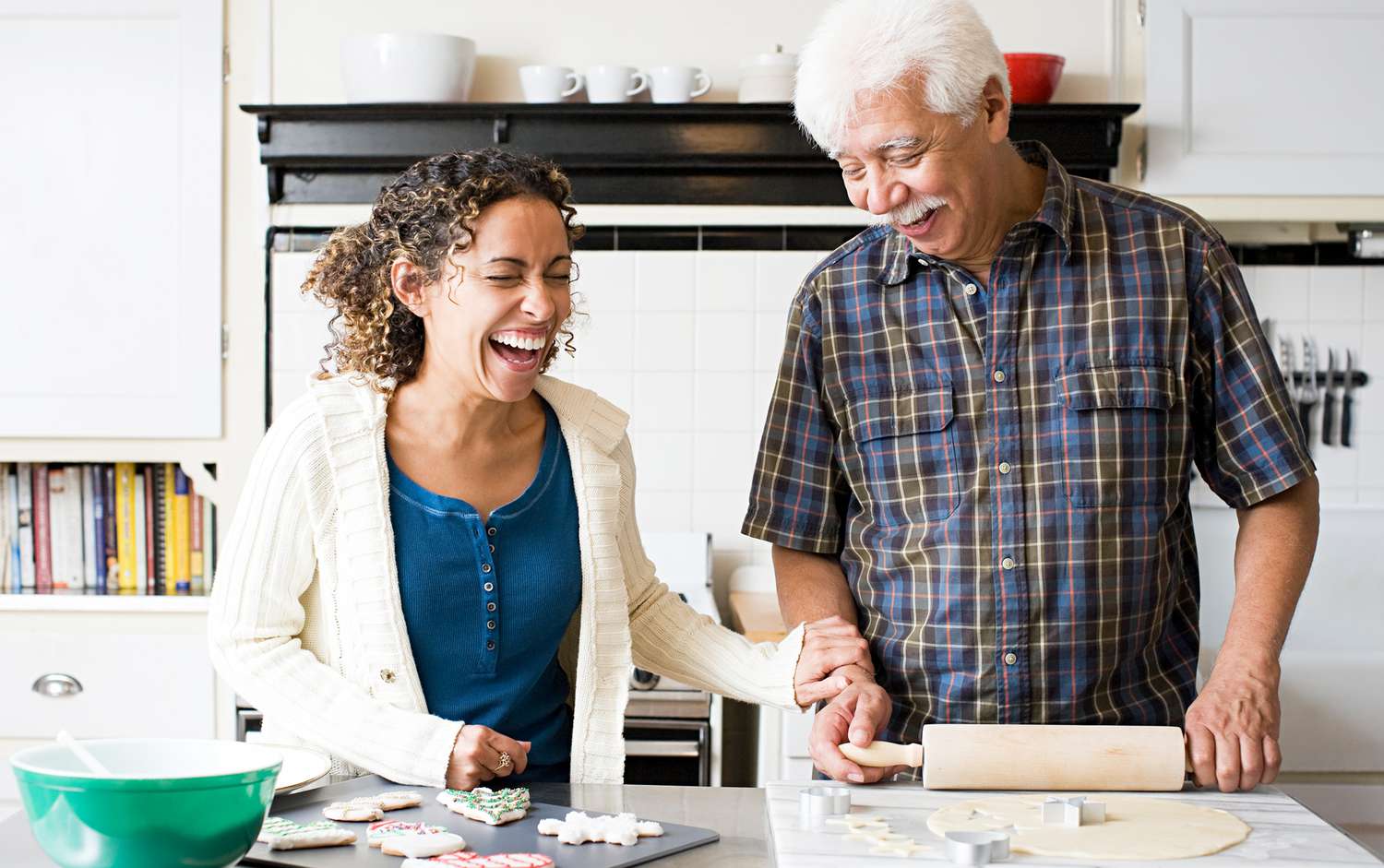 An ethnic father and adult daughter laughing while making cookies