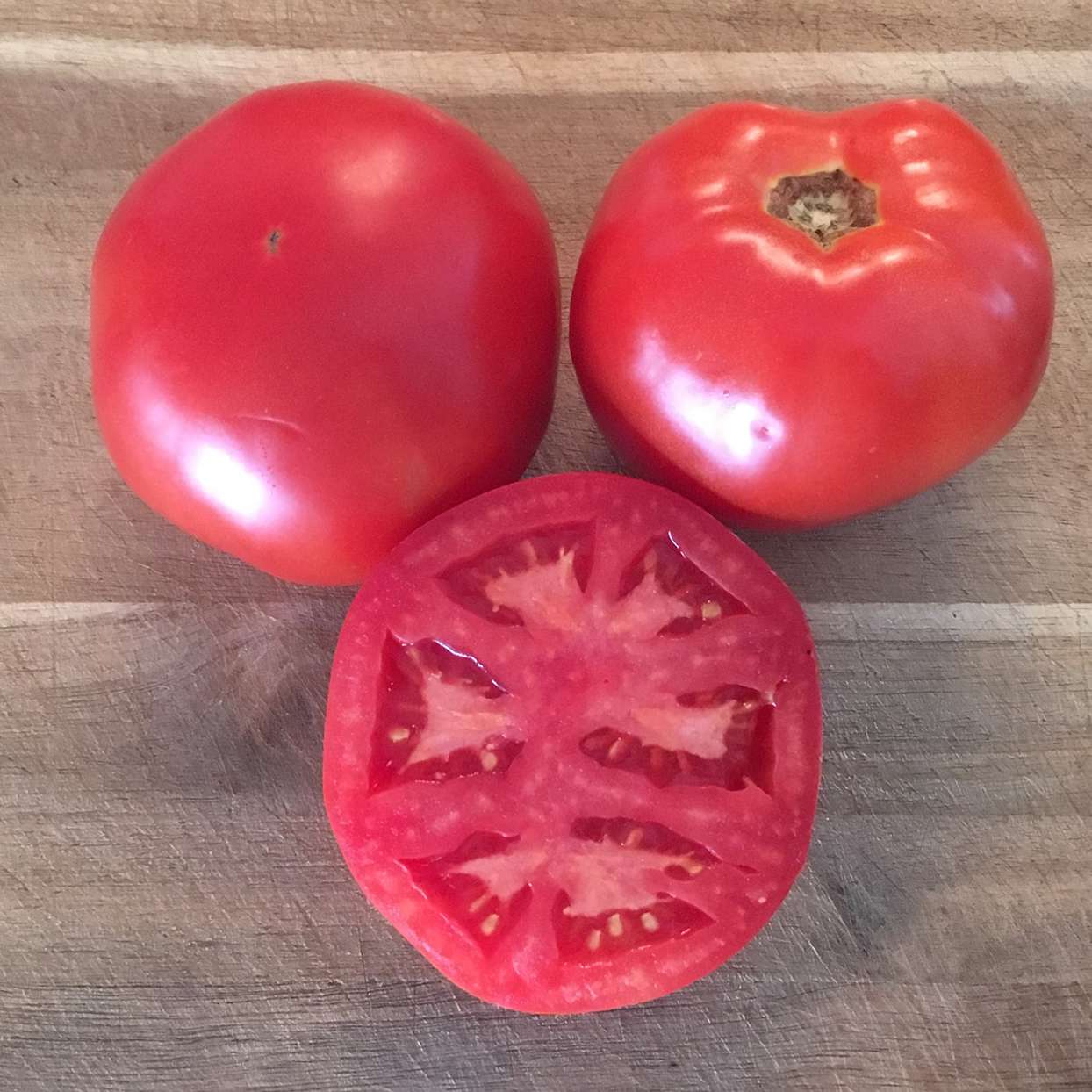three galahad tomatoes on table, one cut in half