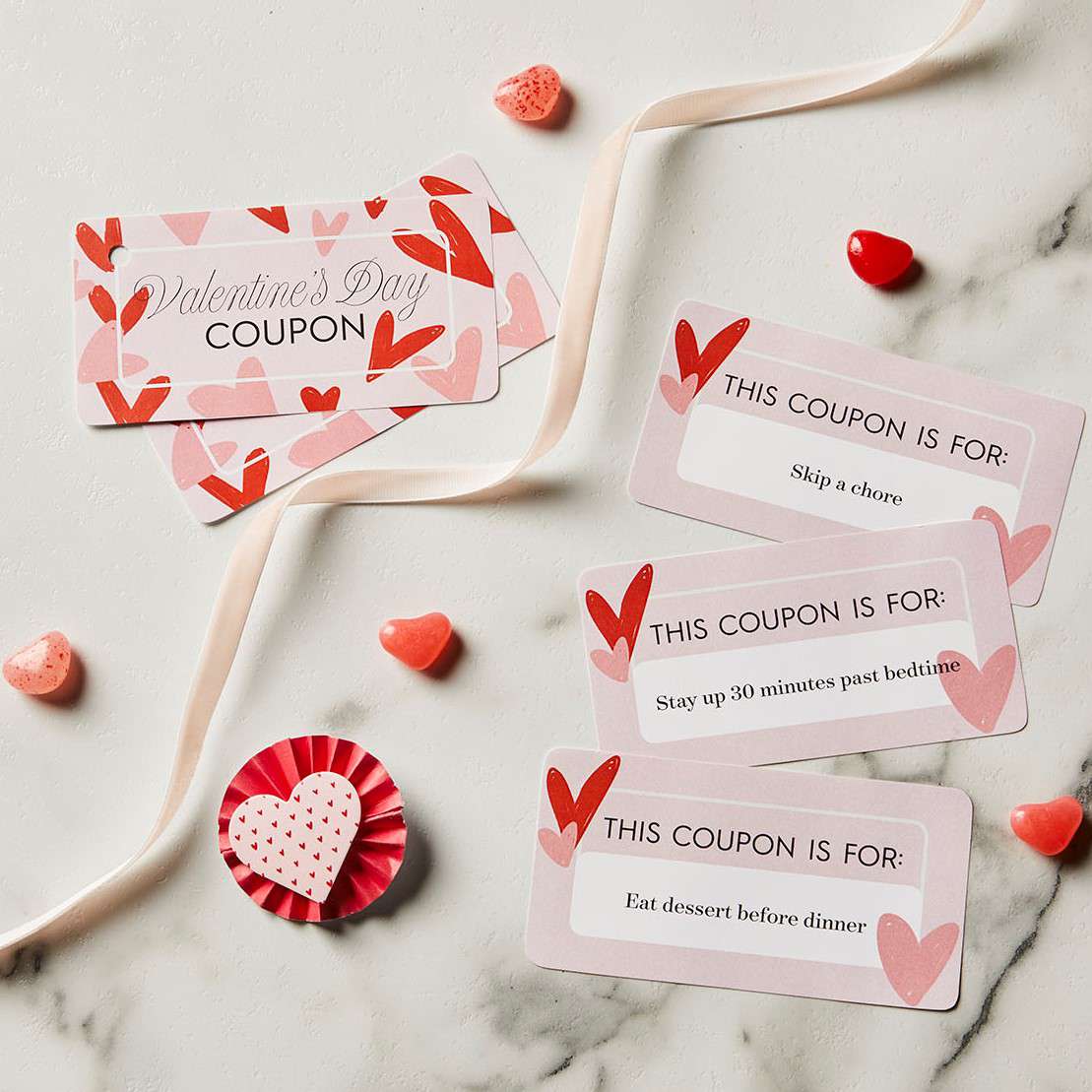 paper valentine's day coupons on a marble surface with pink and red candy