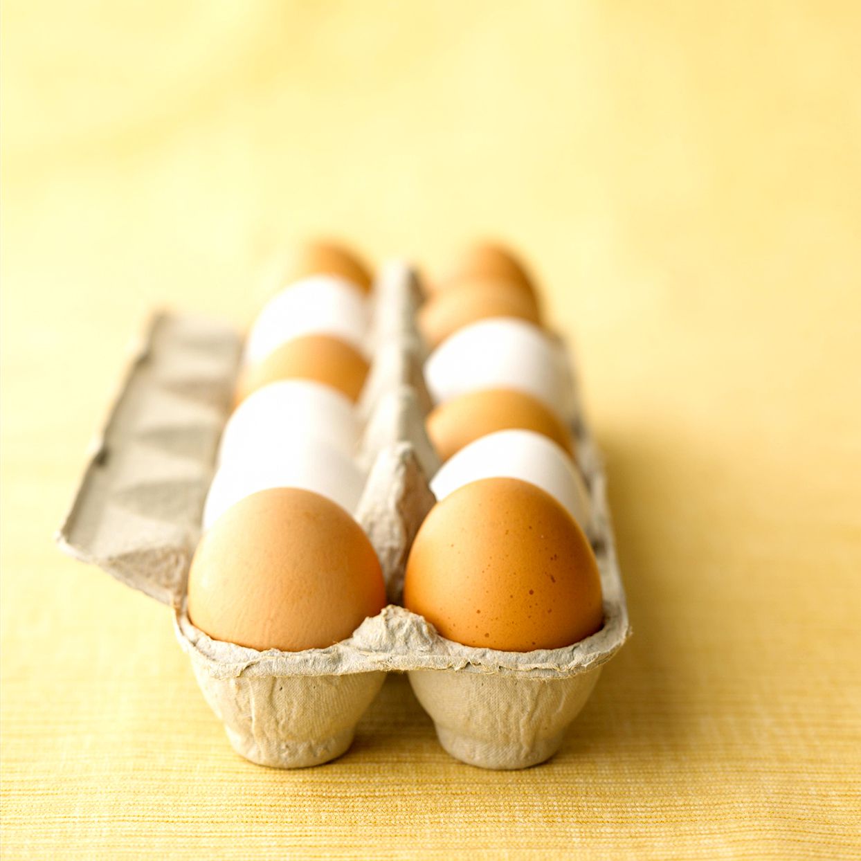 Brown and white eggs in carton on yellow cloth