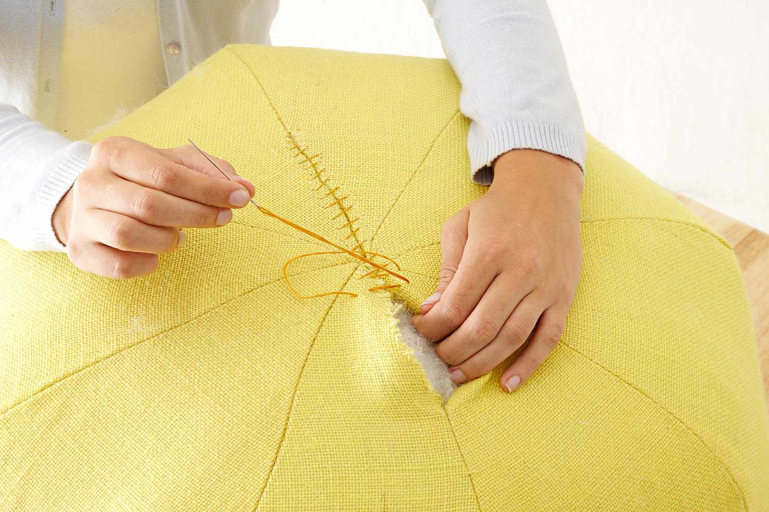 Person sewing top of pouf closed