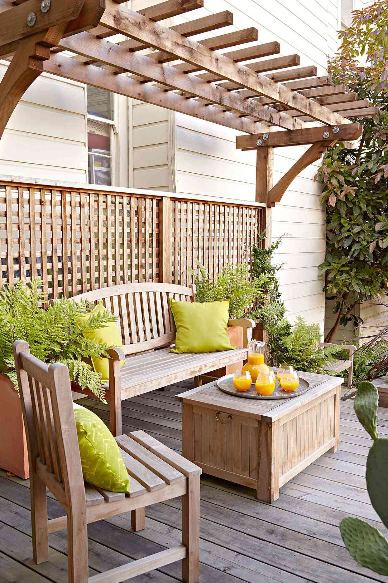 patio furniture and green cushions on deck beneath arbor