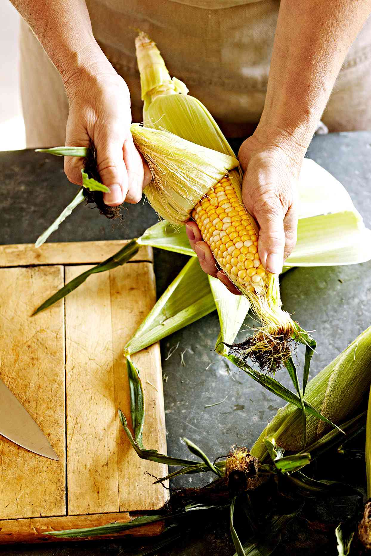 Person shucking corn near cutting board
