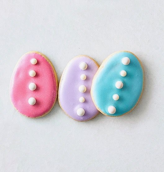 three egg shaped cookies with pastel frosting and edible pearls on top