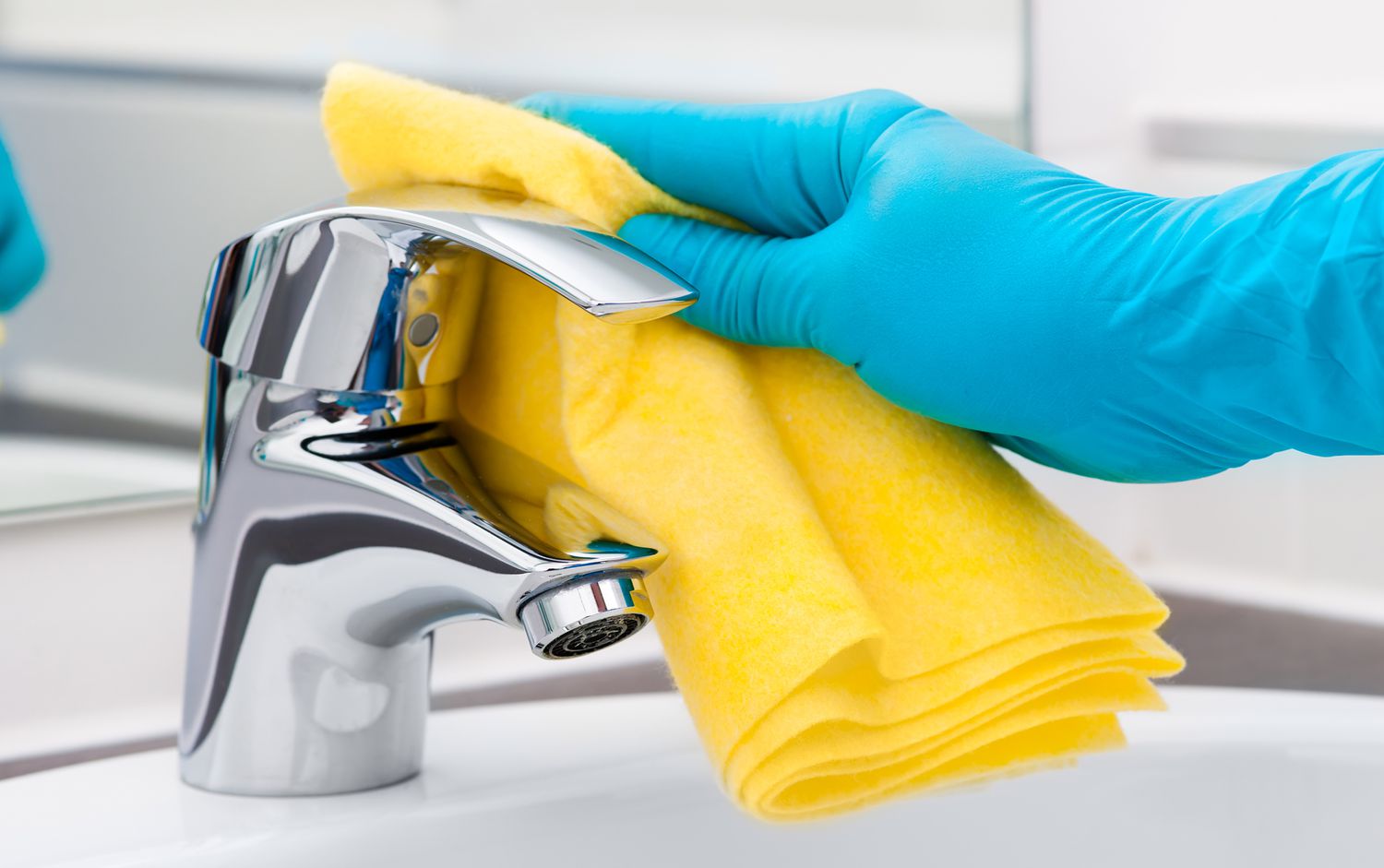 Person cleaning sink with gloves on and a cloth