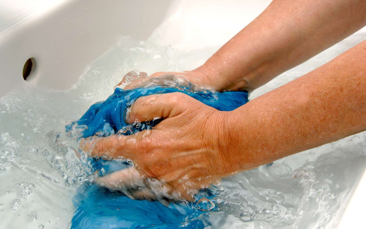 Close up of hands washing clothing in a sink