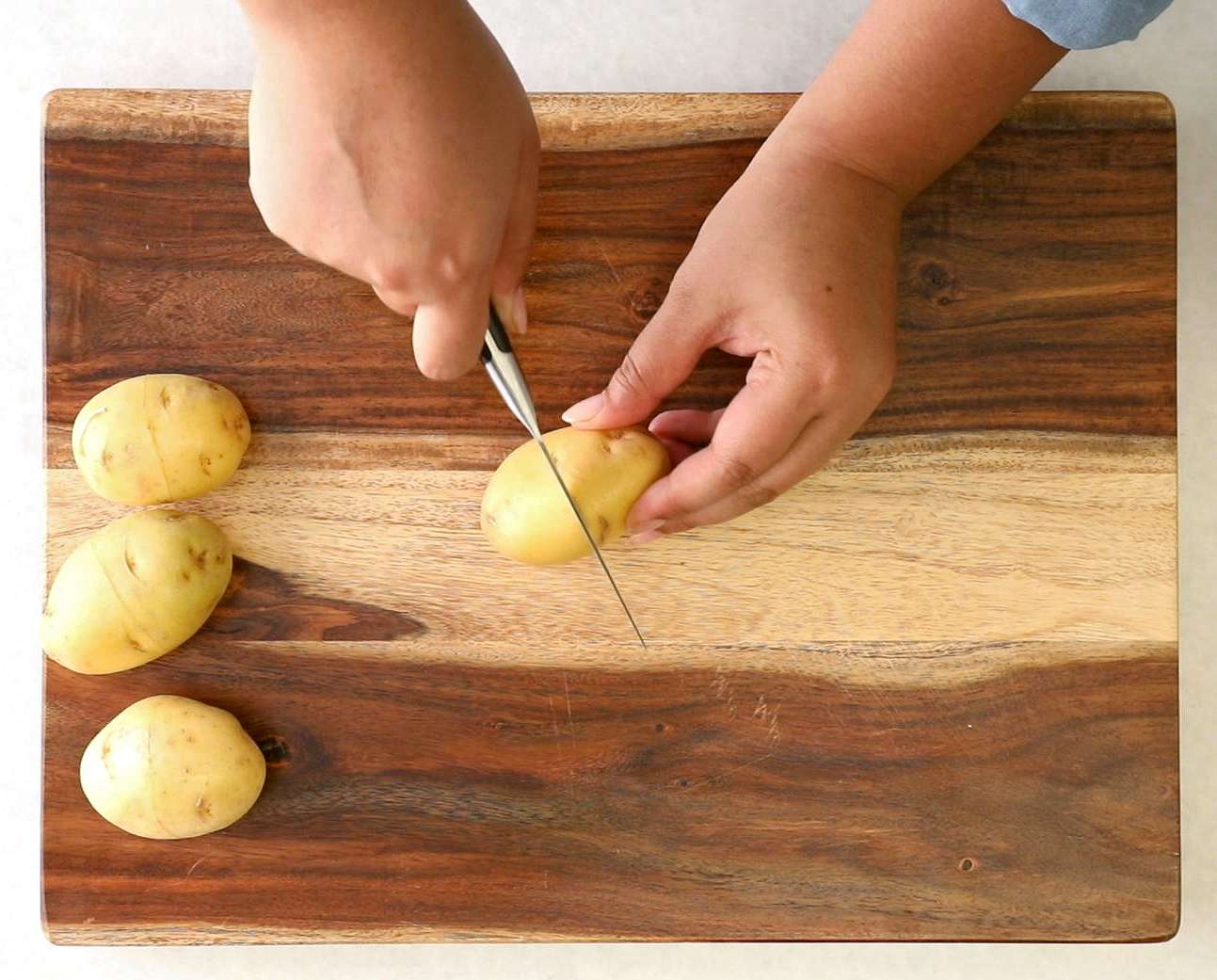 woman cutting small potatoes with paring knife on cutting board