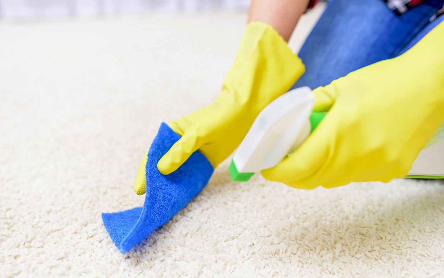 Someone cleaning light carpet with a cloth and spray bottle