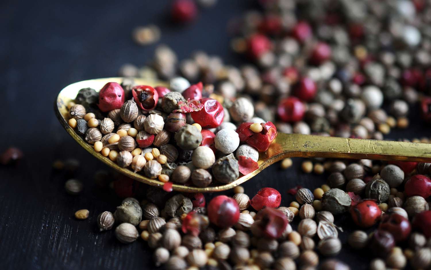 Peppercorns on a gold spoon and dark surface