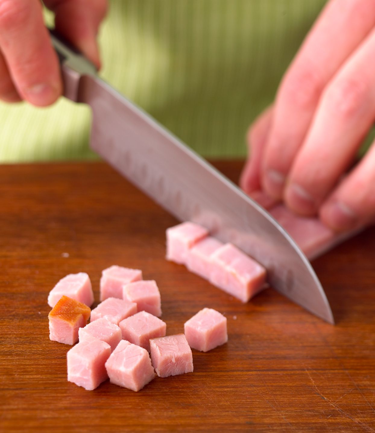 Dicing ham with a chef’s knife on a wooden cutting board