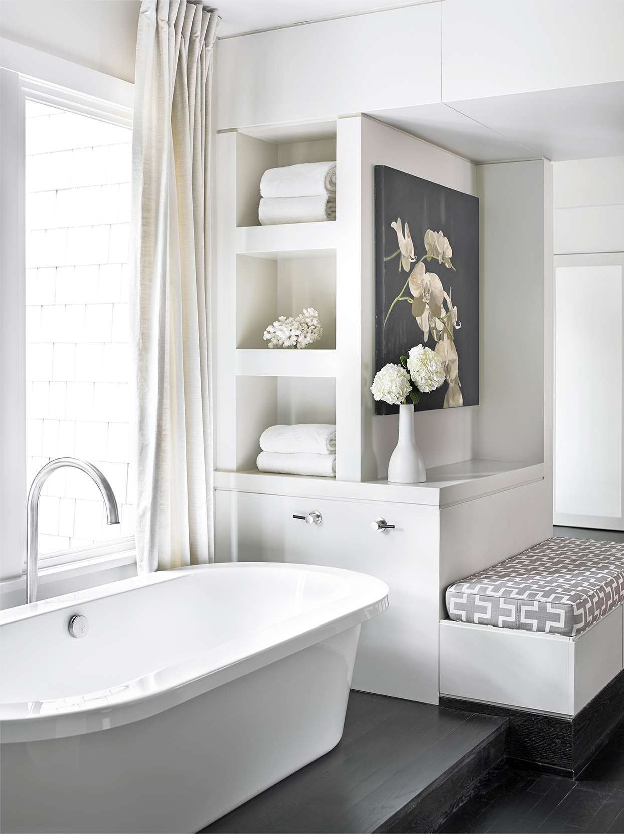 White bathroom with tub, bench, storage and floral artwork