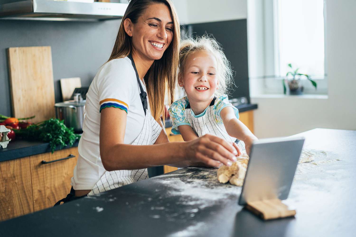 mother and daughter baking together in modern kitchen and using digital tablet for recipe