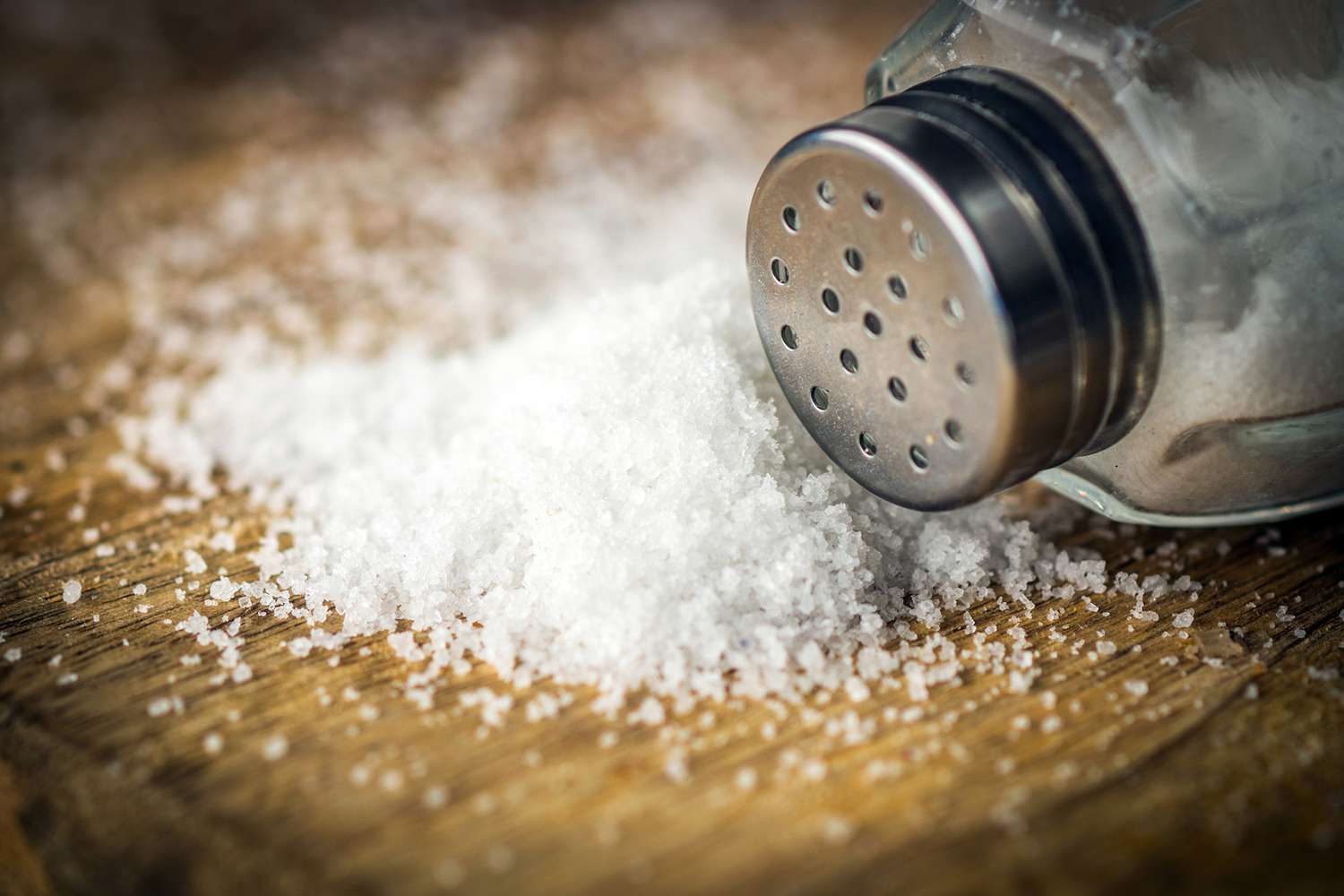 salt shaker with spilled pile of salt on wooden background
