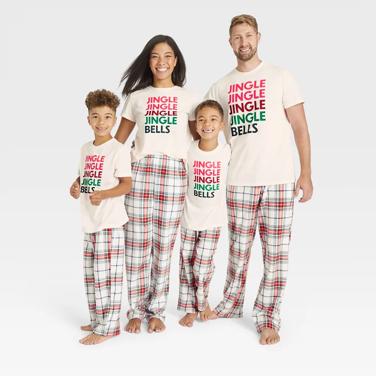 happy family of four wearing matching plaid pajama bottoms and jingle bells themed t-shirts