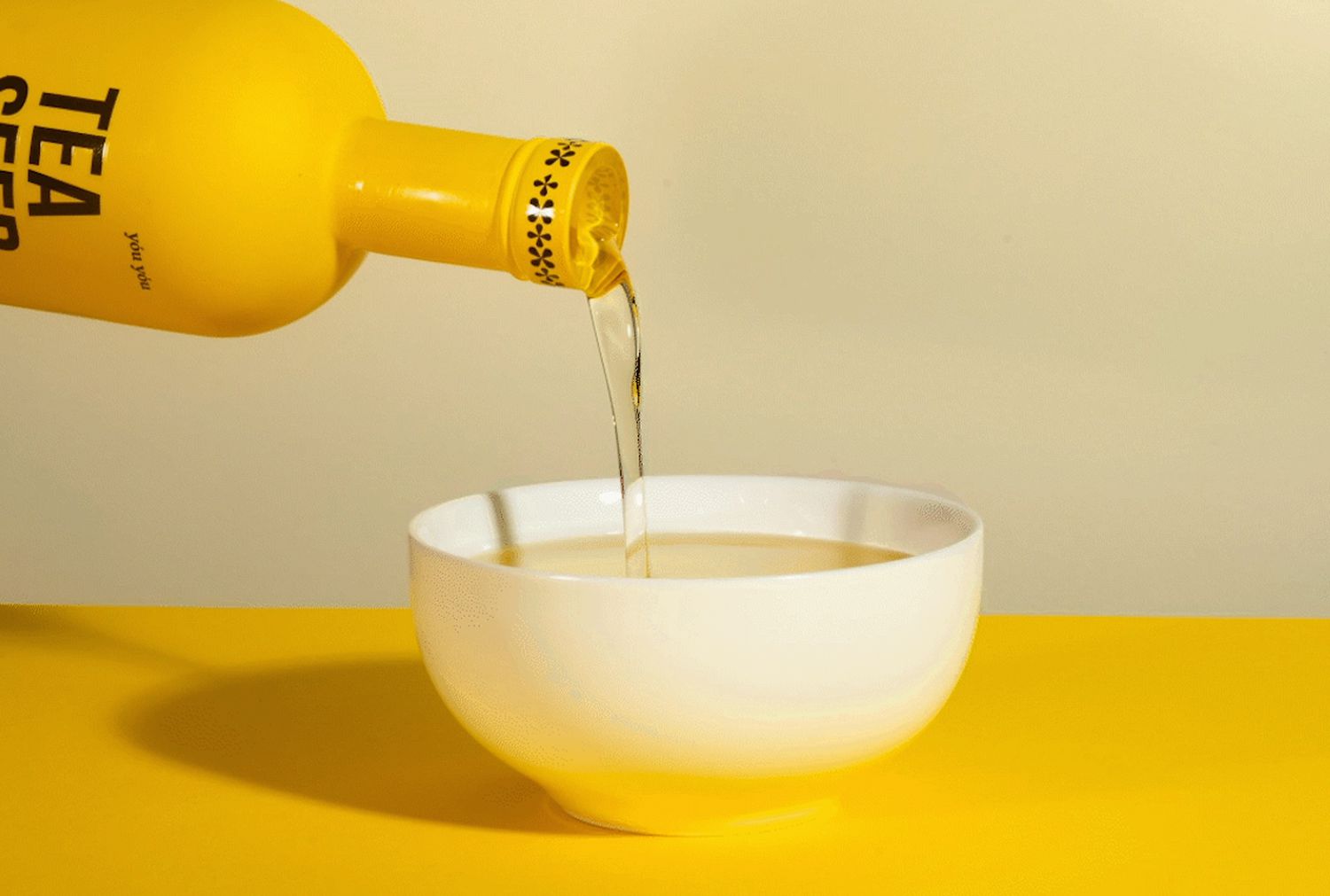 bottle of tea seed oil pouring into white dish against yellow background