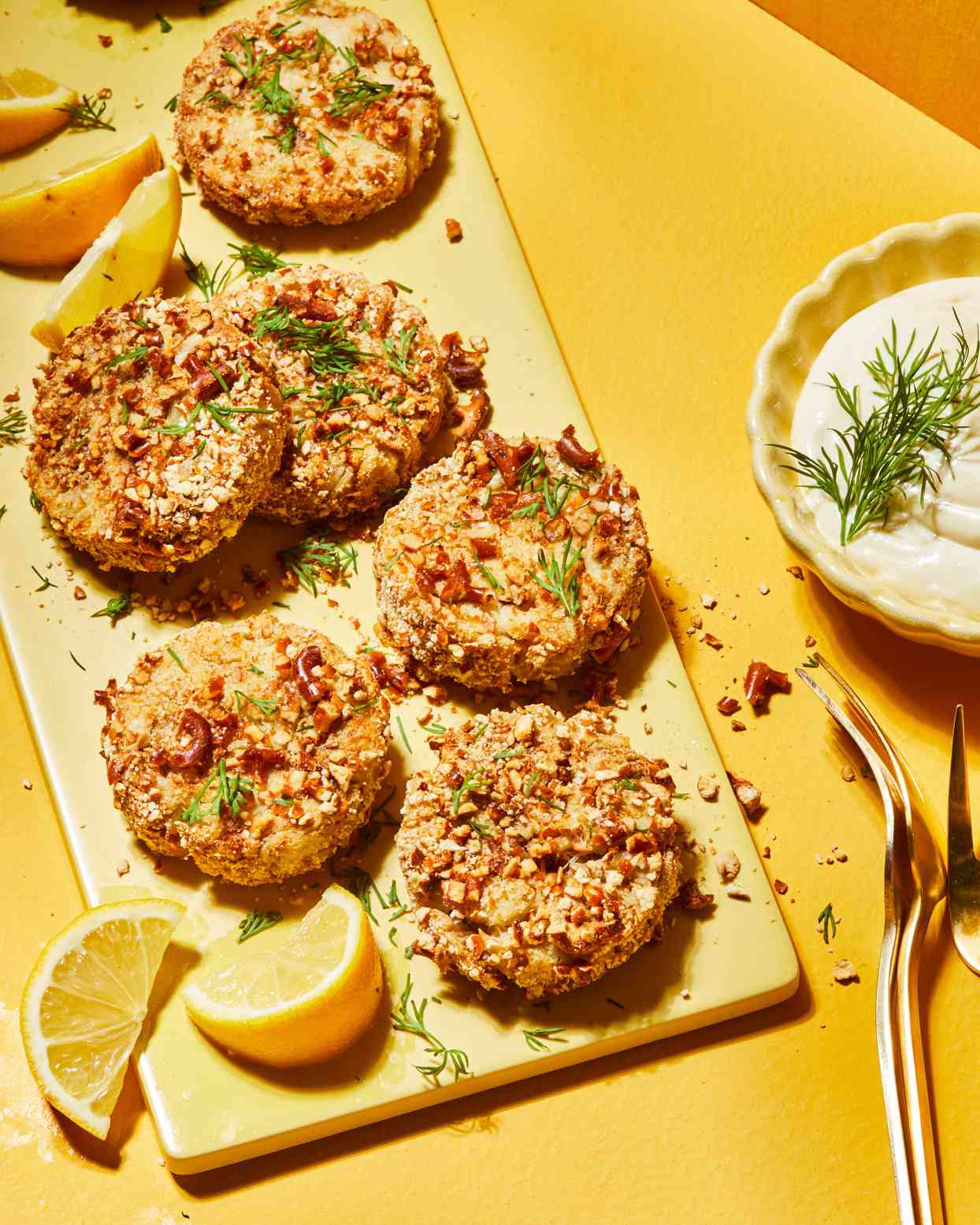Pretzel-Crusted Crab Cakes on board with lemon wedges and dill garnish