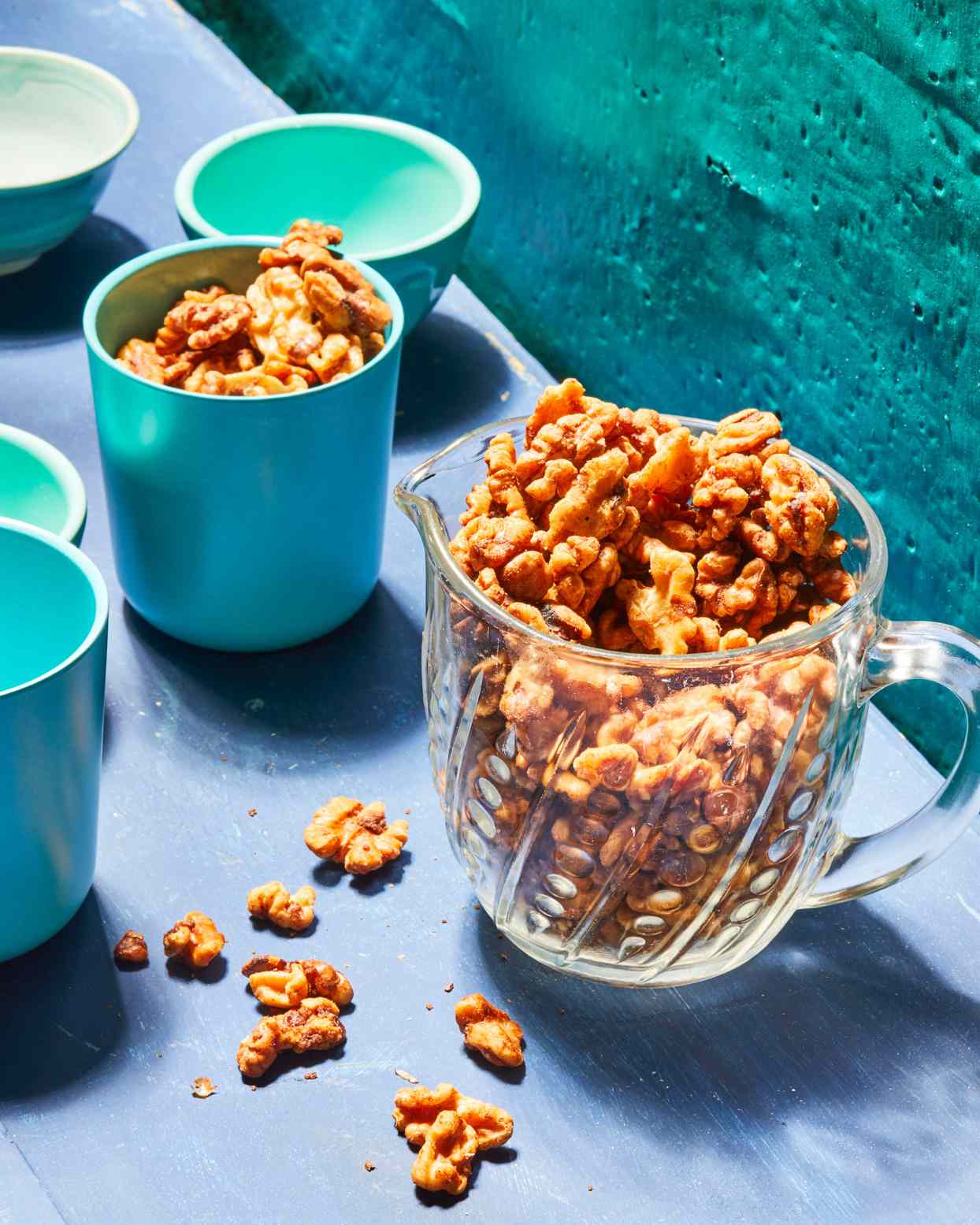 glass dish of spiced walnuts on blue background