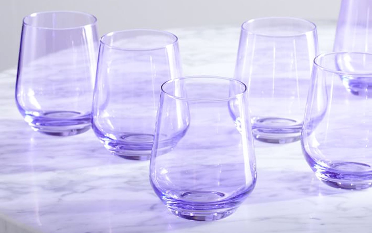 Multiple lavender colored stemless wine glasses on a marble surface