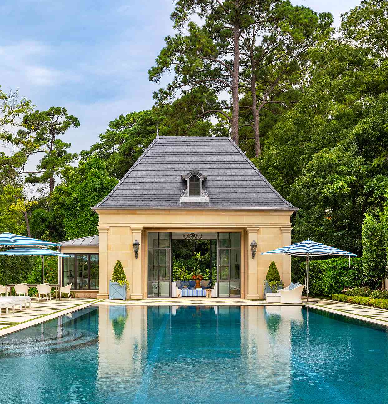 french chateau-inspired pool house blue striped umbrellas trees