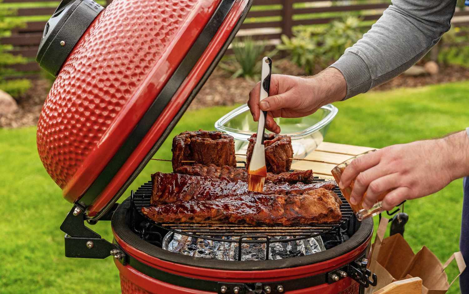 A person is brushing bbq sauce on ribs on a red smoker grill