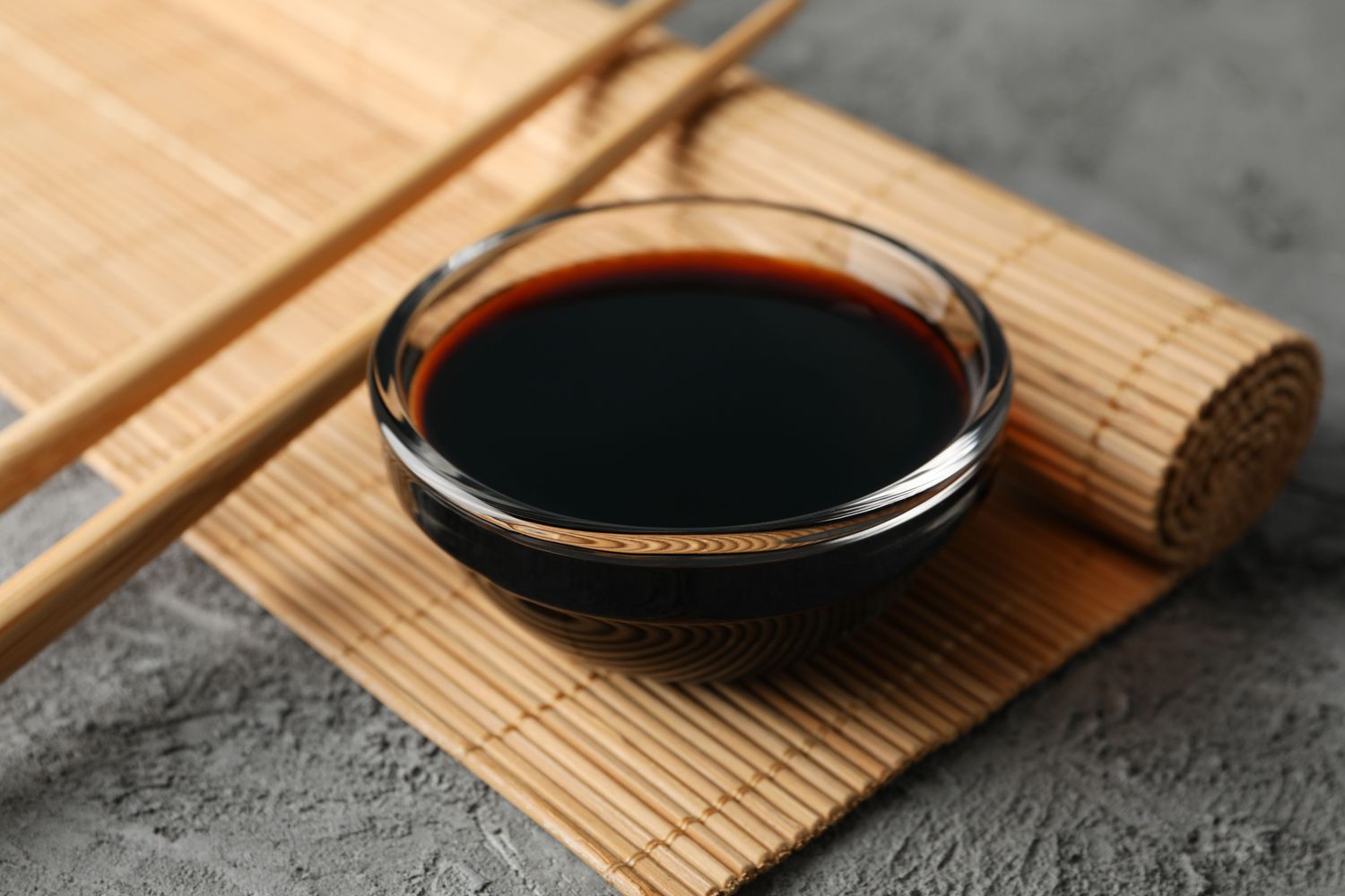 small bowl of soy sauce on Japanese sushi rolling mat with chopsticks