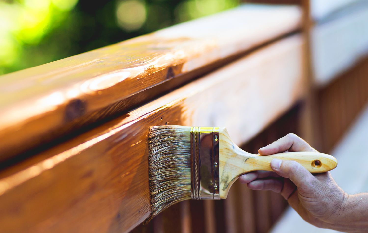 person applying deck stain to wooden deck railing