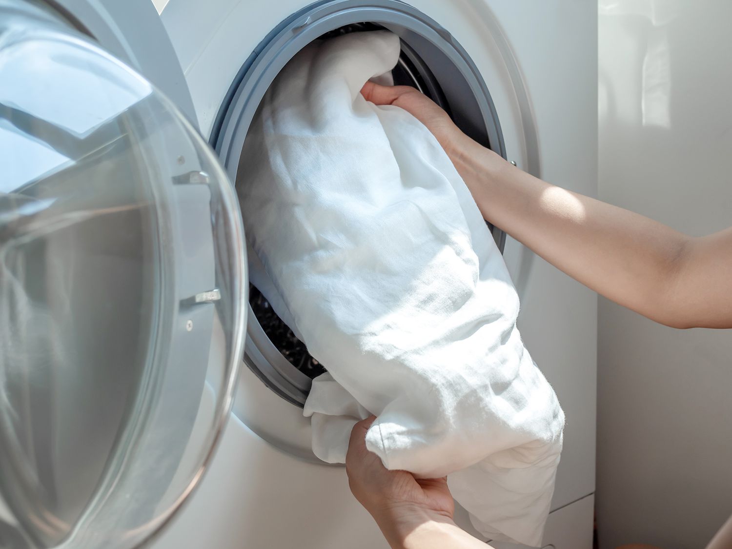 close up of person doing laundry loading white sheet into washer