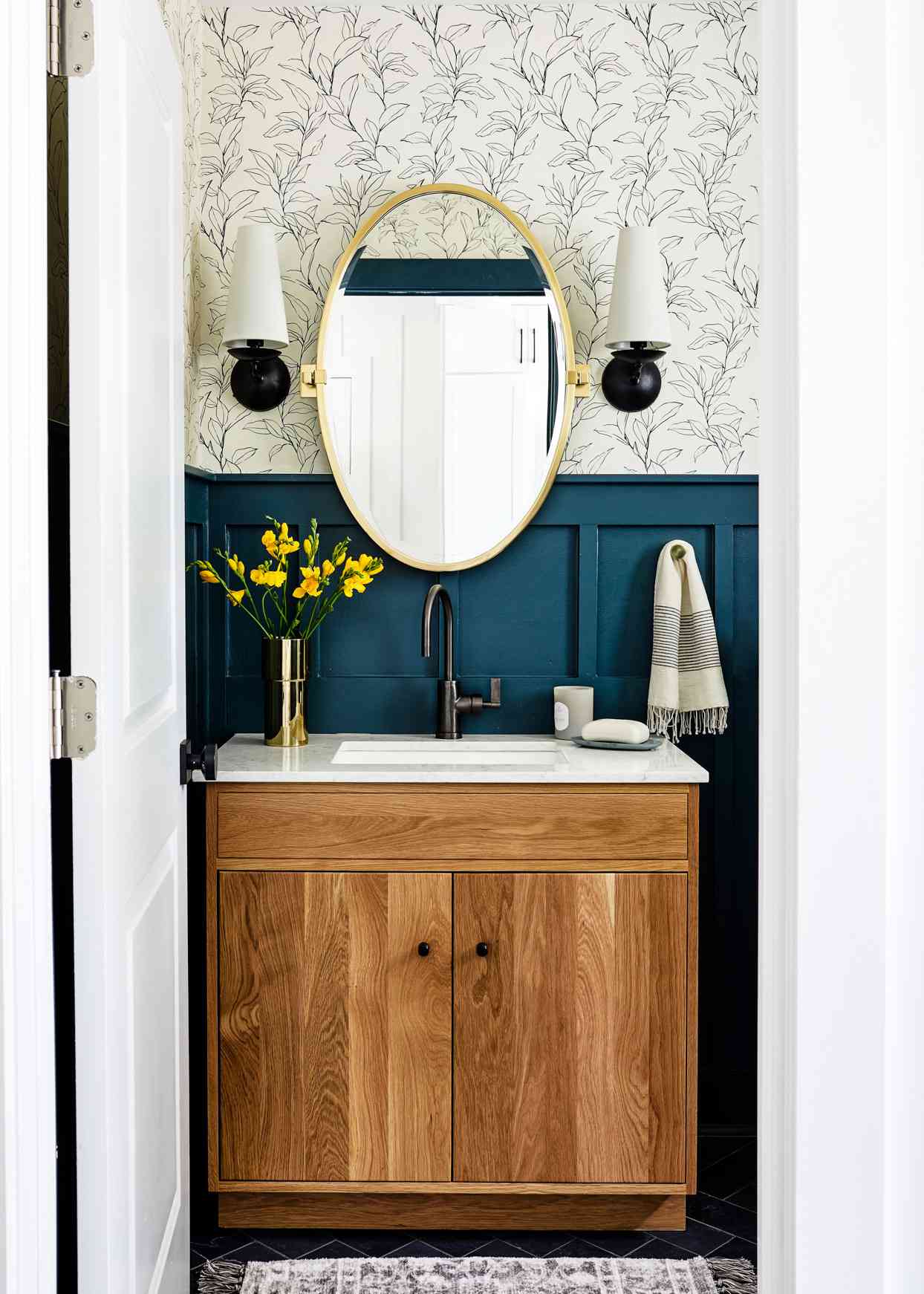 wallpapered bathroom with black sconces and wooden vanity