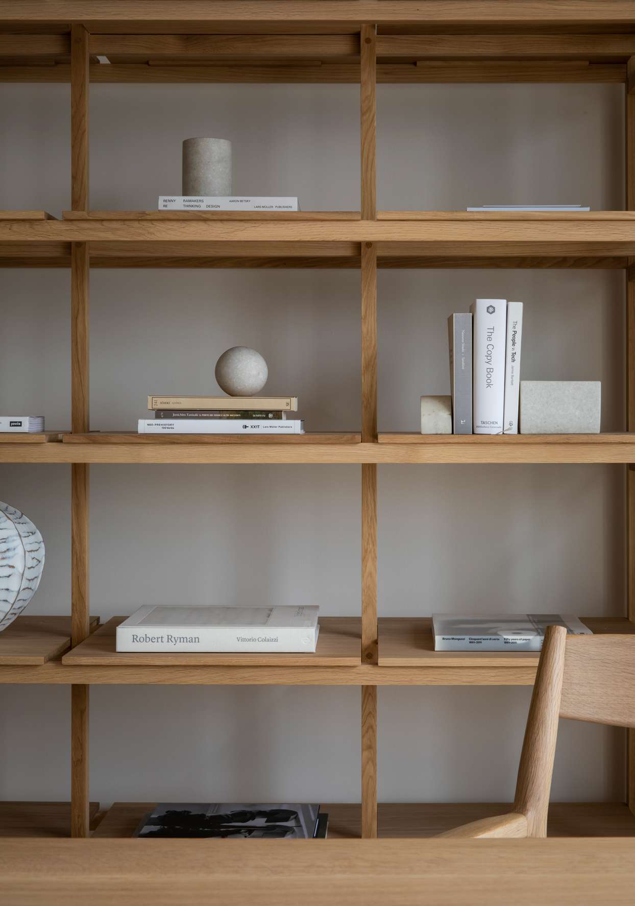 minimally decorated wooden bookshelf with art objects, books and wooden chair