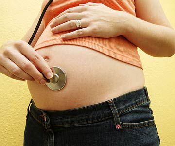hands holding stethoscope on pregnant belly