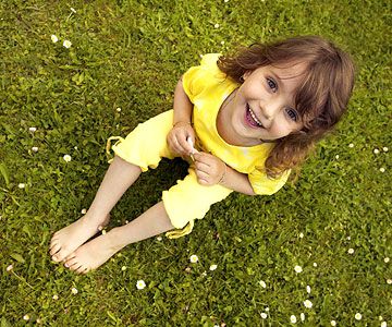 Little girl with gold earrings sitting on grass, holding white flower