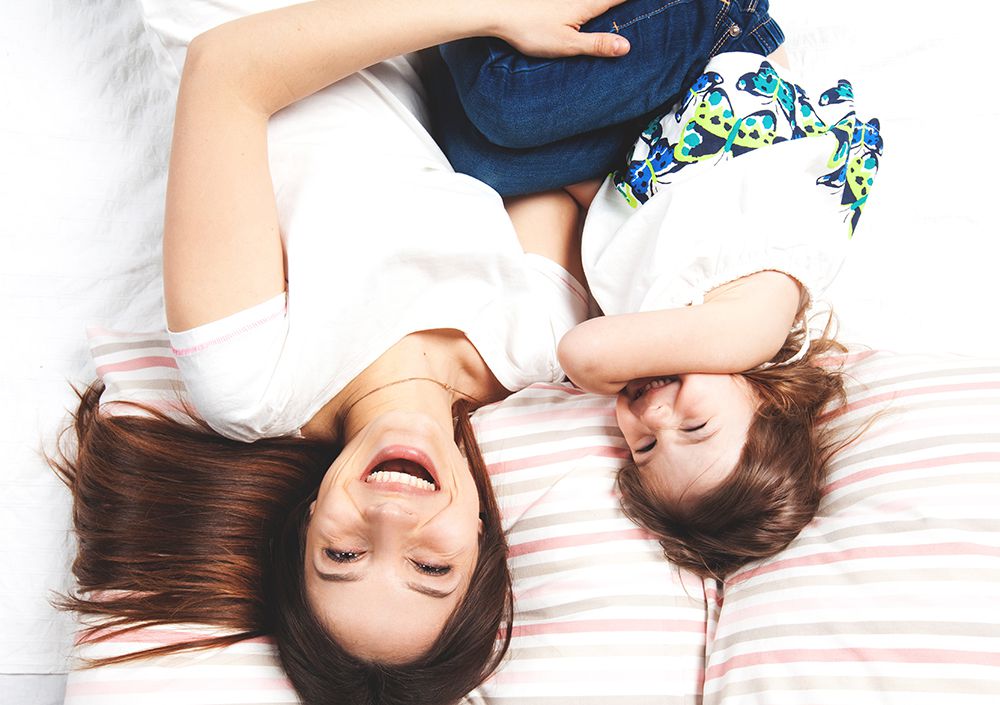 mom and toddler daughter laying on bed laughing